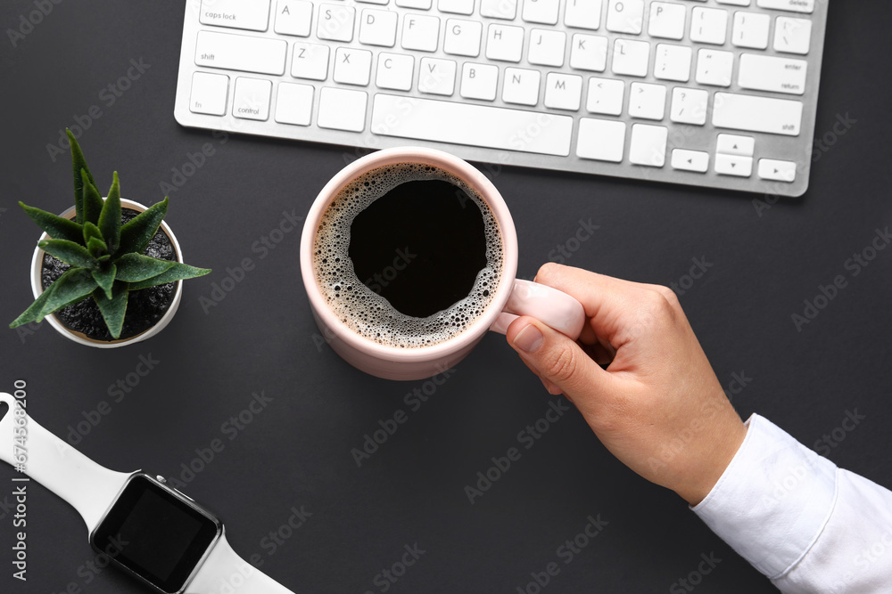 Woman holding cup of hot coffee and keyboard on black background