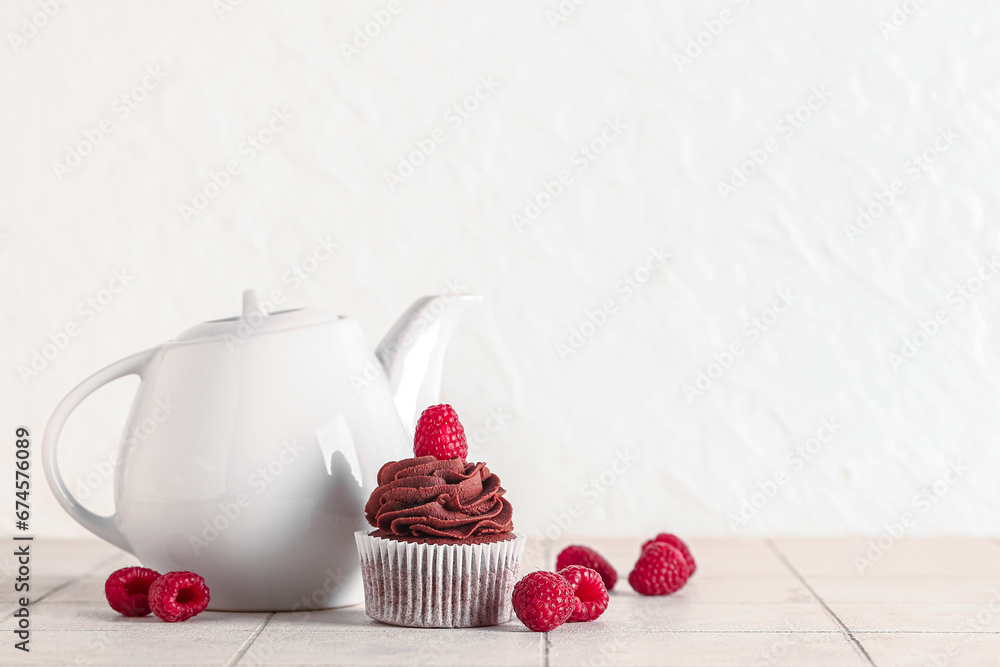 Tasty chocolate cupcake with raspberries and teapot on table