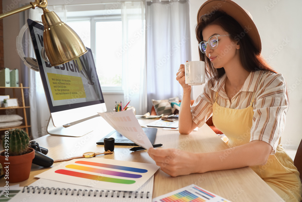 Female interior designer with cup of coffee working at table in office