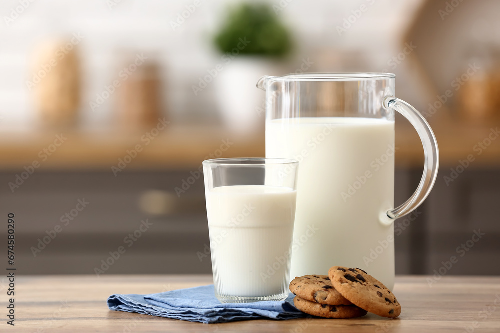 Glass and jug of fresh milk with sweet cookies on wooden table in kitchen