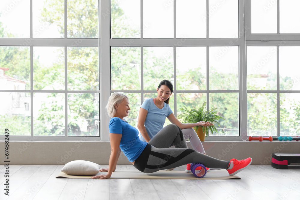 Mature woman training with therapist on mat in rehabilitation center