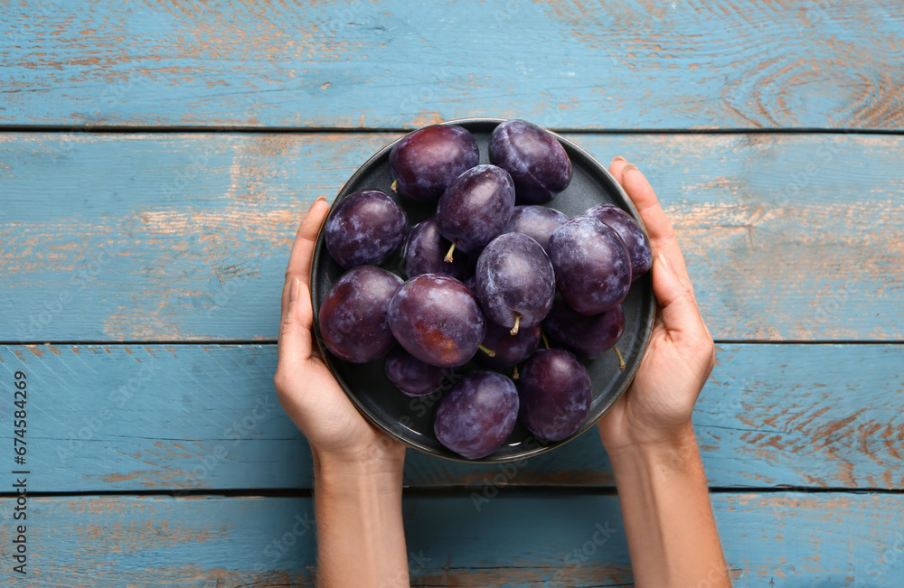 Woman holding plate with fresh plums on blue wooden background