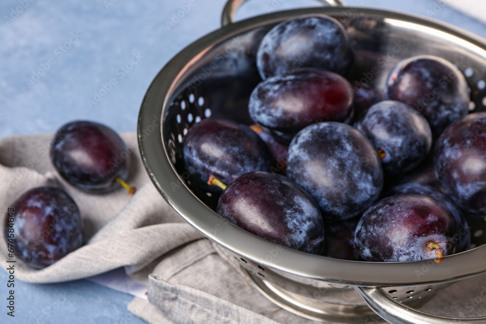 Colander with fresh plums on blue background