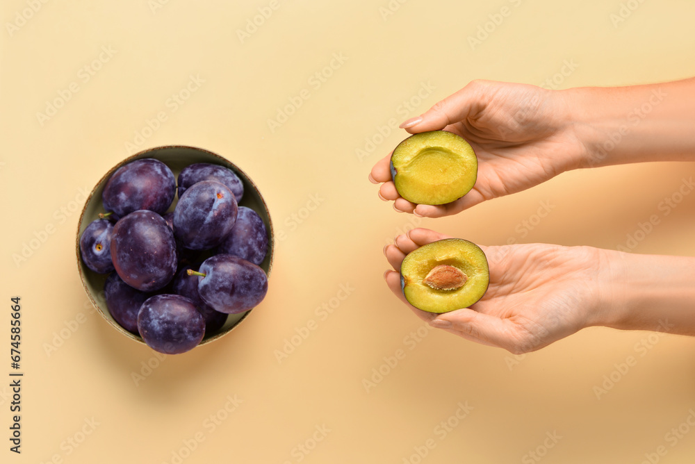 Woman holding halves of fresh plum on yellow background