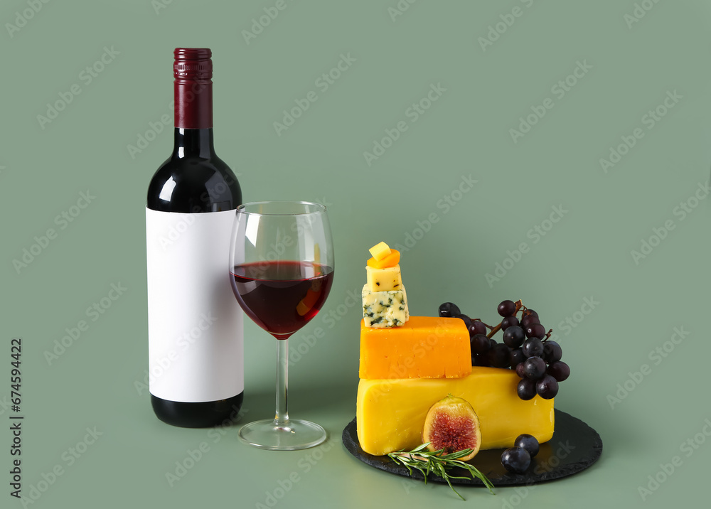 Board with tasty cheese, grapes, bottle and glass of wine on green background