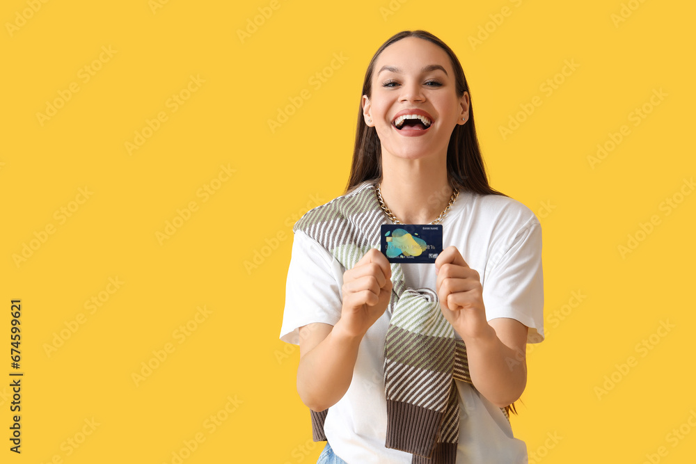 Young woman with credit card on yellow background