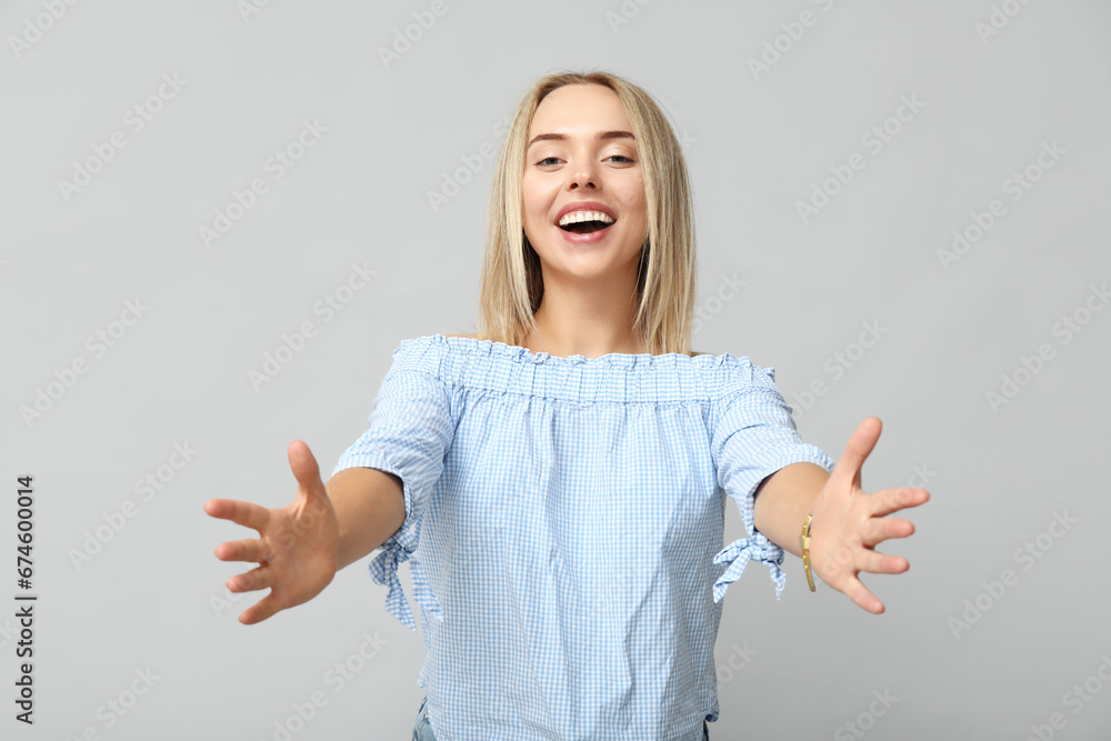 Young woman opening arms for hug on grey background