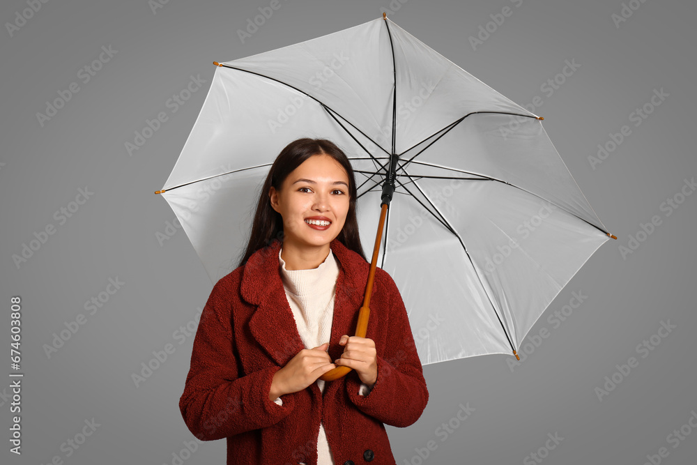 Beautiful young Asian woman with umbrella on grey background