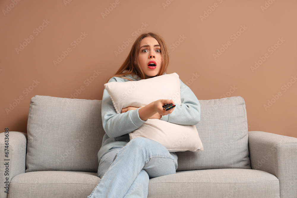 Scared young woman with TV remote control watching movie in living room