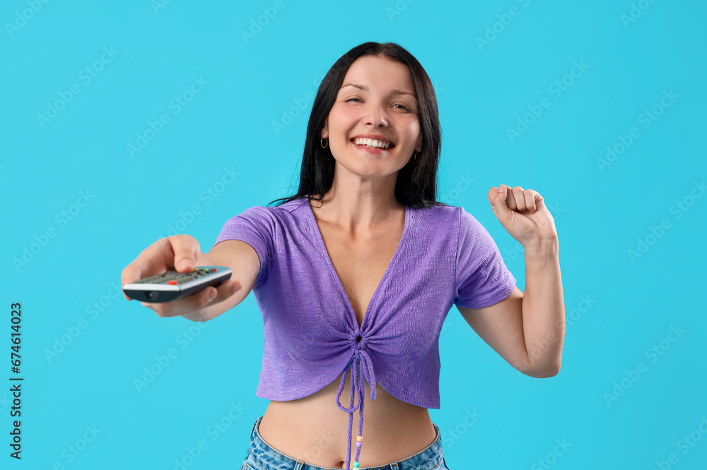 Joyful young woman with remote control watching TV on blue background