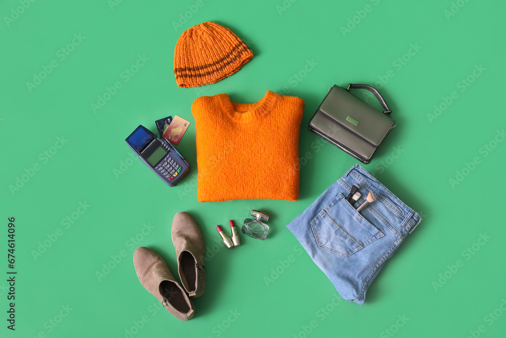 Winter clothes with accessories, payment terminal and credit cards on green background