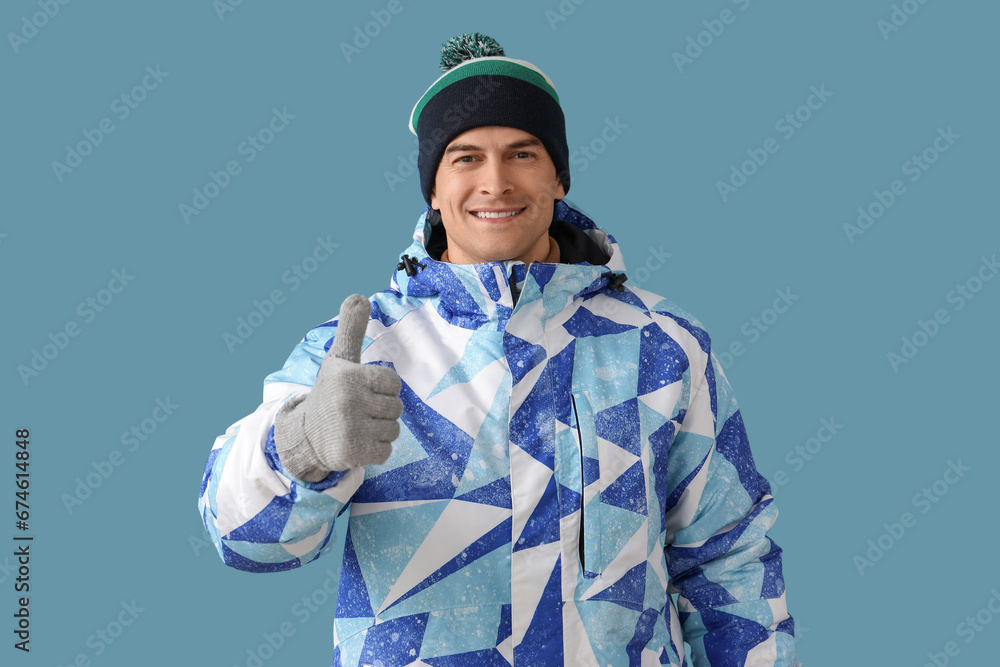 Handsome man in winter clothes showing thumb-up on blue background