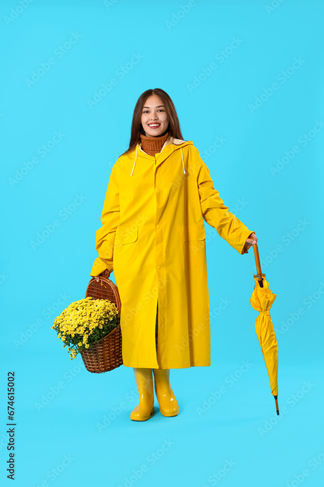 Young Asian woman with chrysanthemum flowers and umbrella on blue background