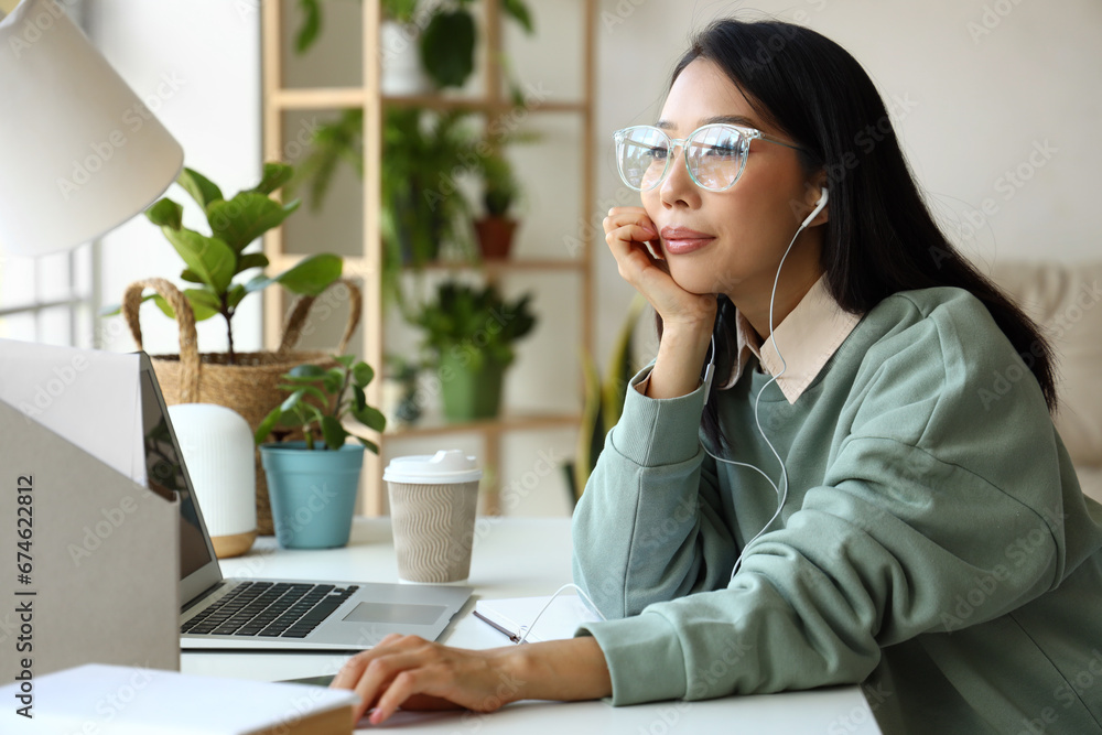 Young Asian woman in earphones working at home office