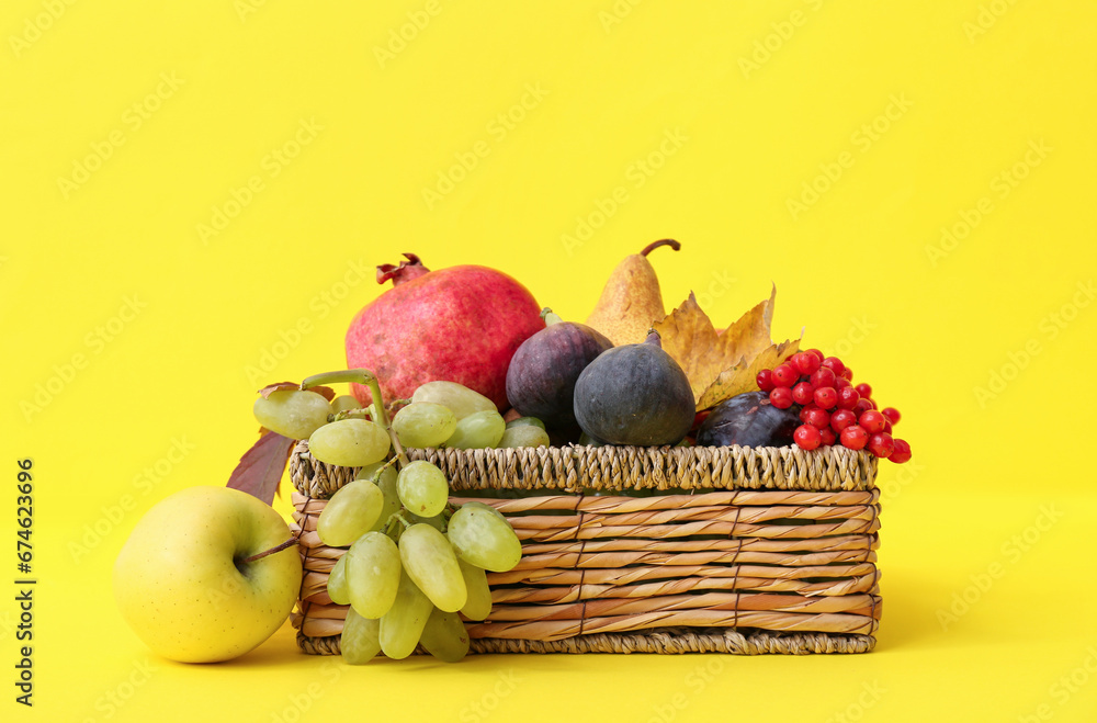 Wicker basket with different fresh fruits on yellow background