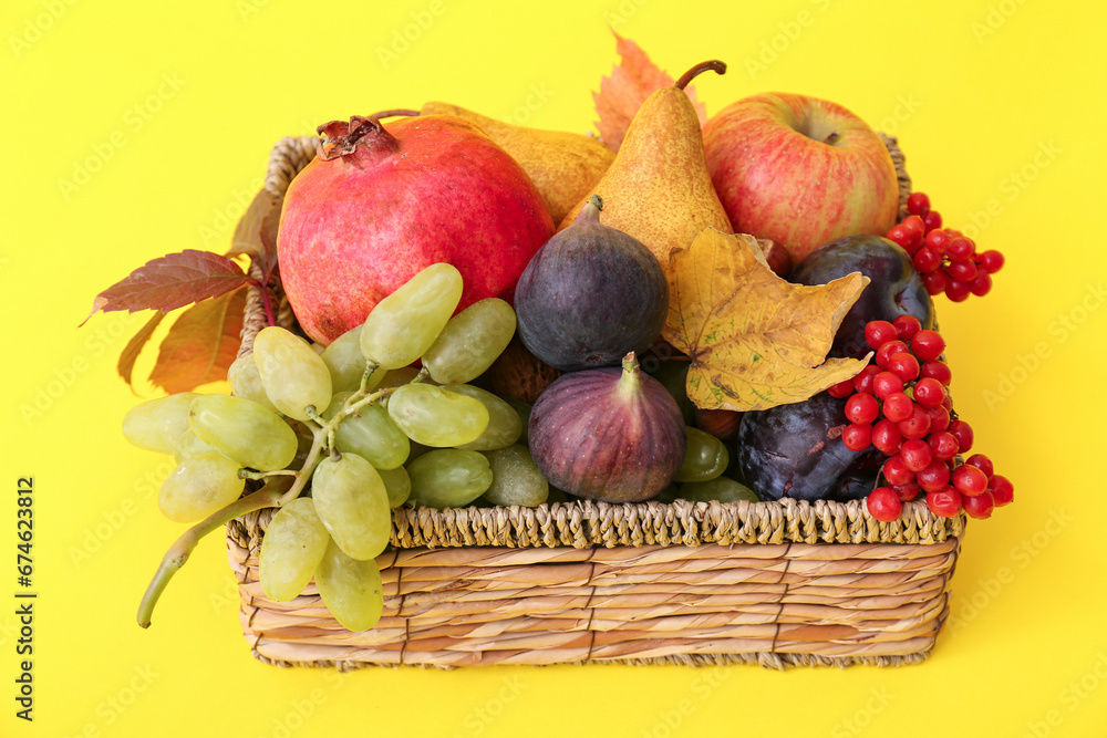 Wicker basket with different fresh fruits on yellow background