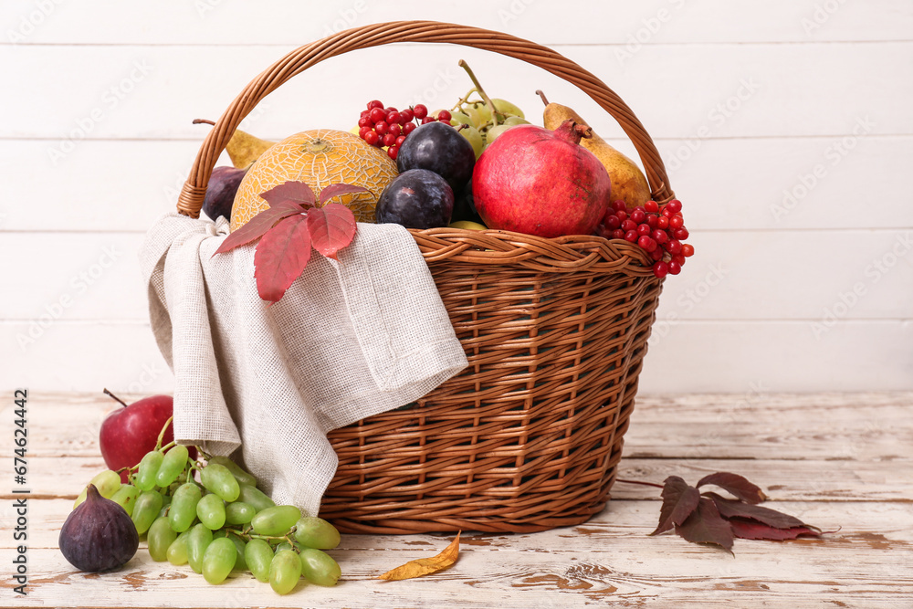 Wicker basket with different fresh fruits on white wooden background