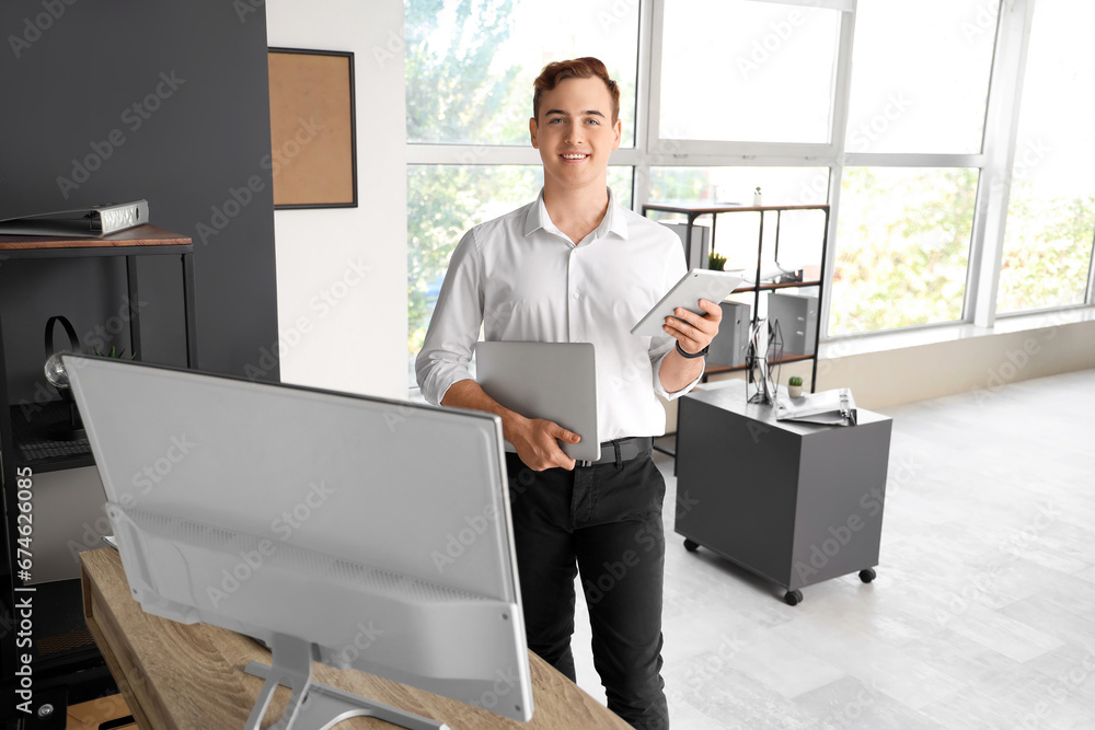 Young businessman with laptop and tablet computer in office