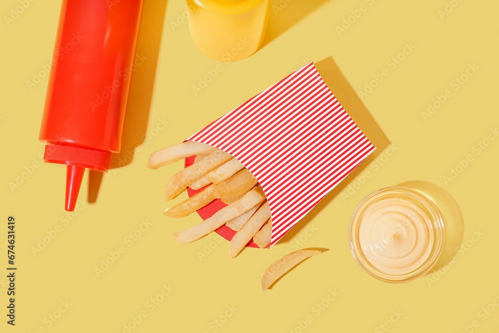 Paper box with french fries and sauces on yellow background