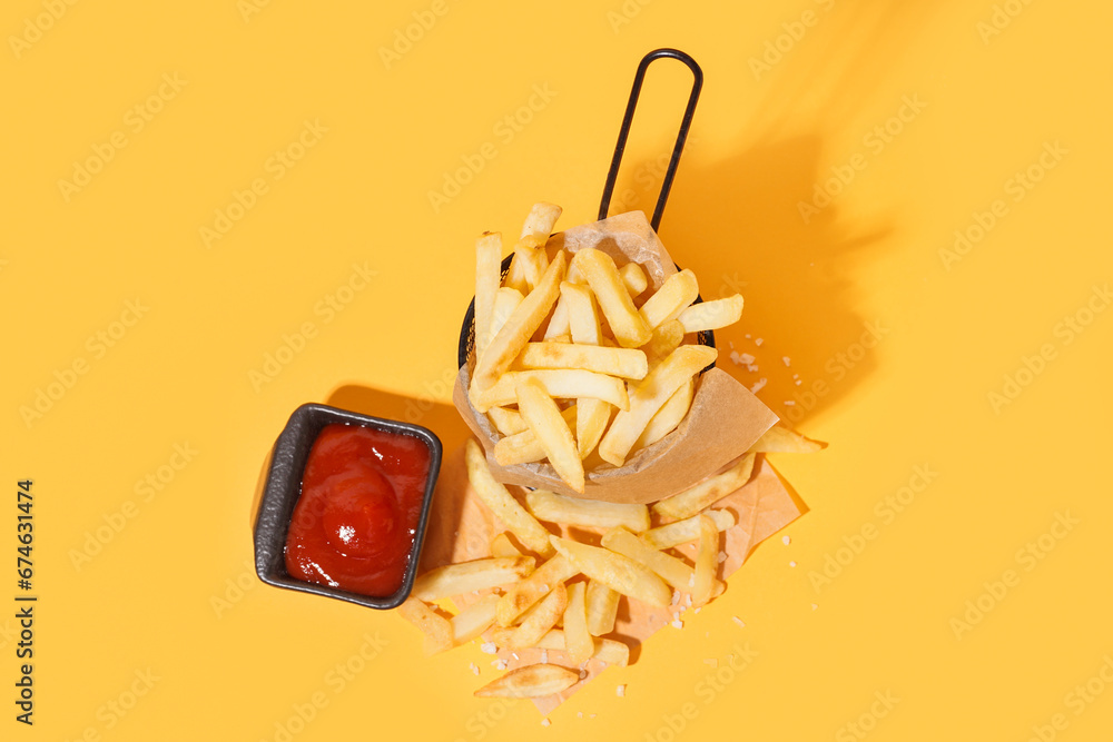 French fries in metal basket with ketchup on orange background