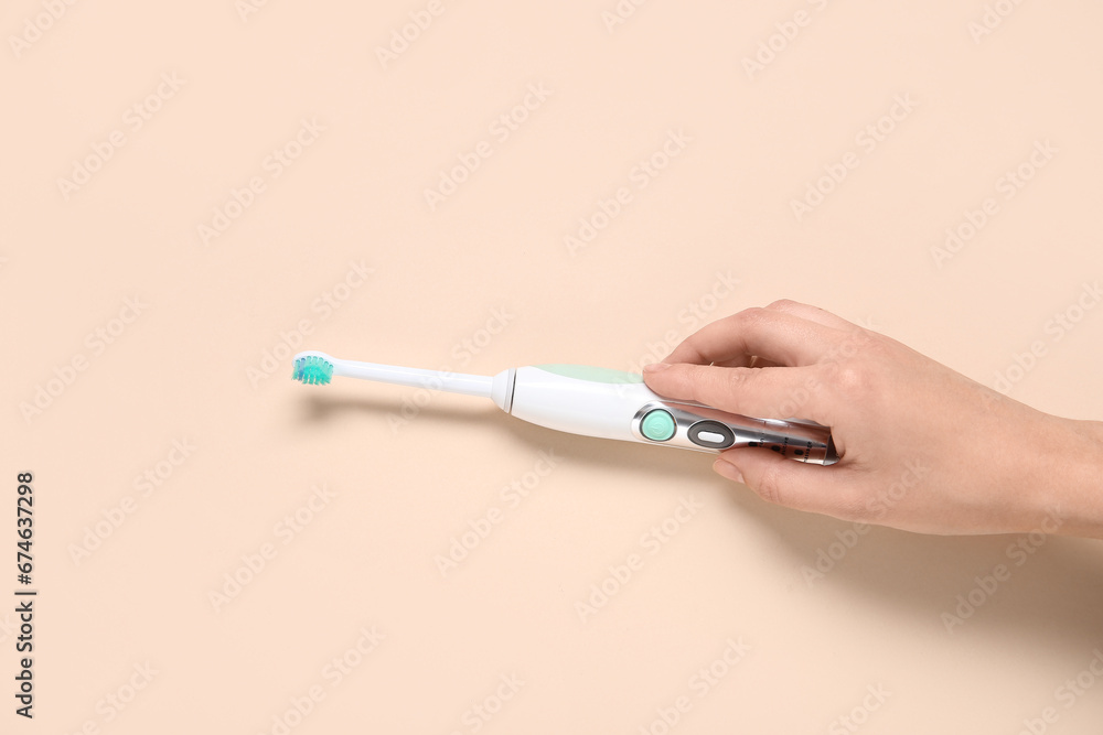 Female hand with electric toothbrush on beige background.