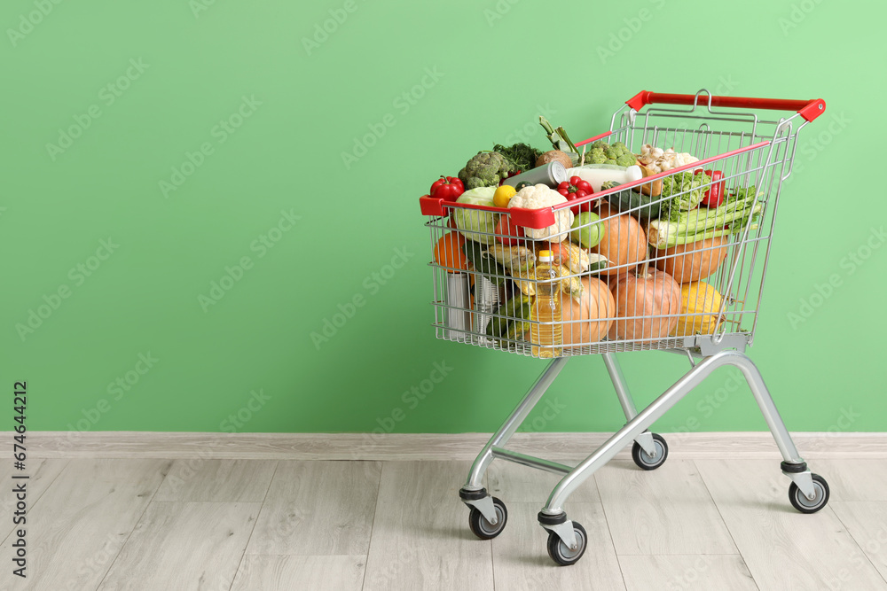 Shopping cart full of food near green wall