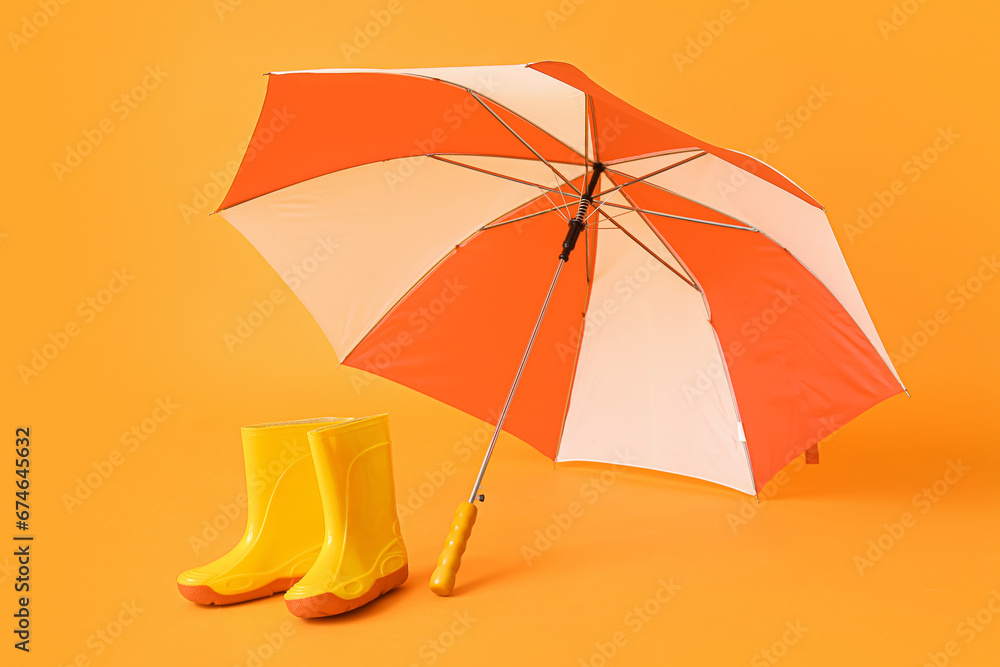 Colorful stylish umbrella and gumboots on orange background