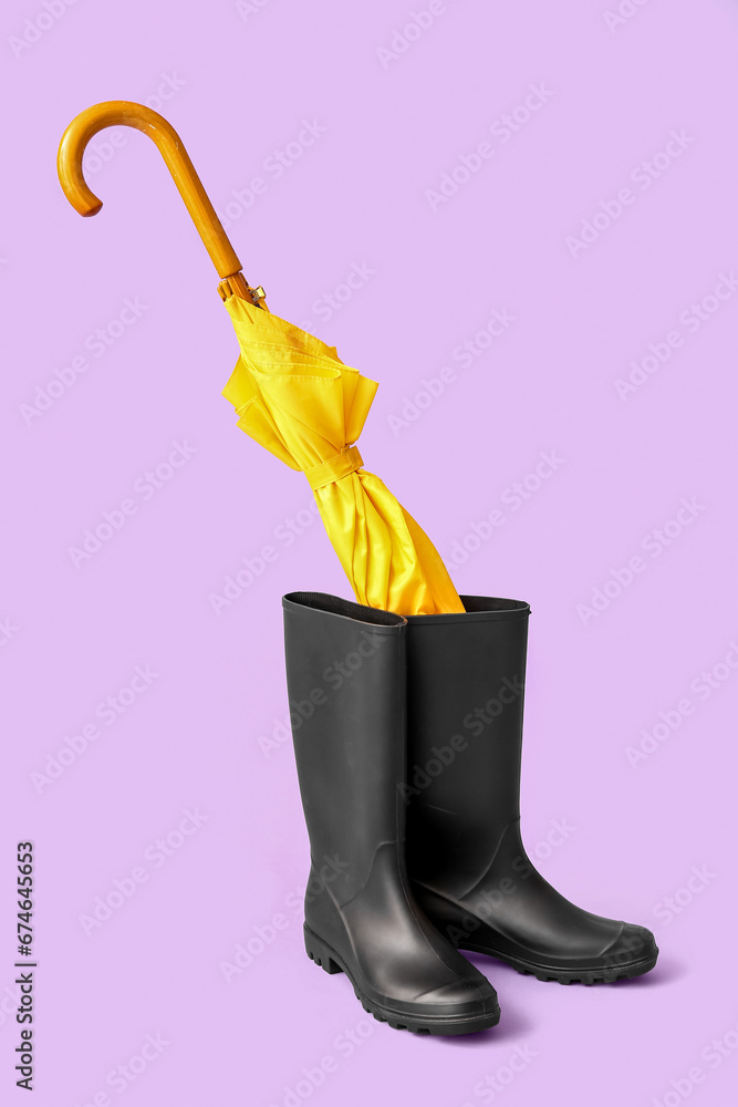 Yellow stylish umbrella and gumboots on lilac background