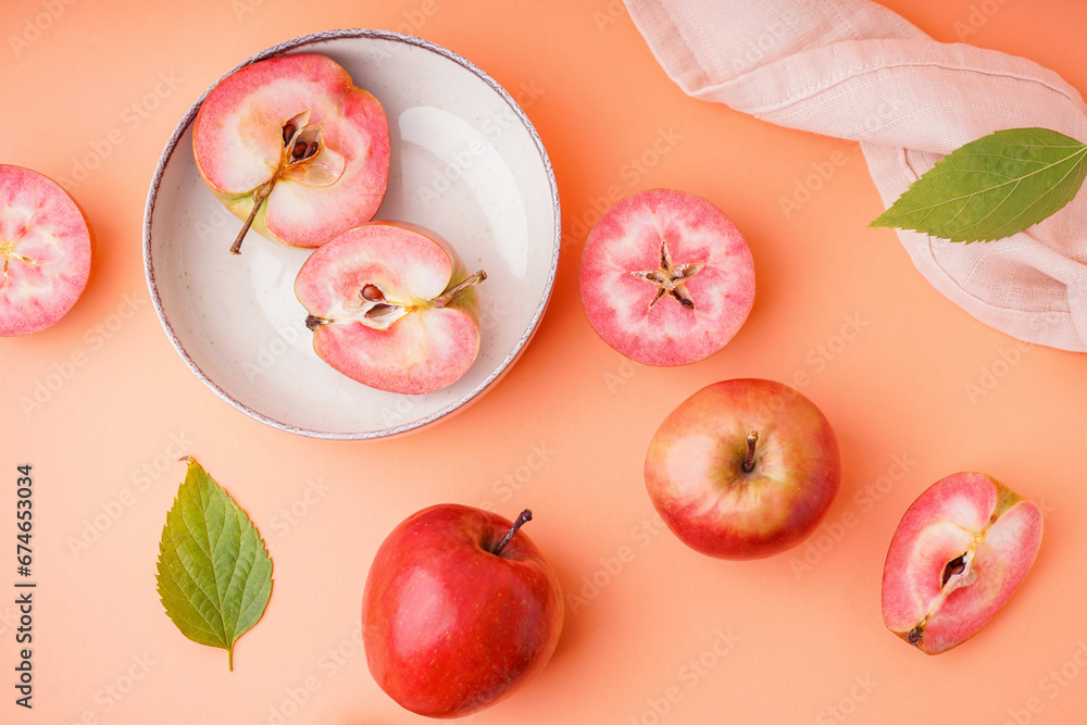 Plate with halves of sweet pink apple and leaves on orange background