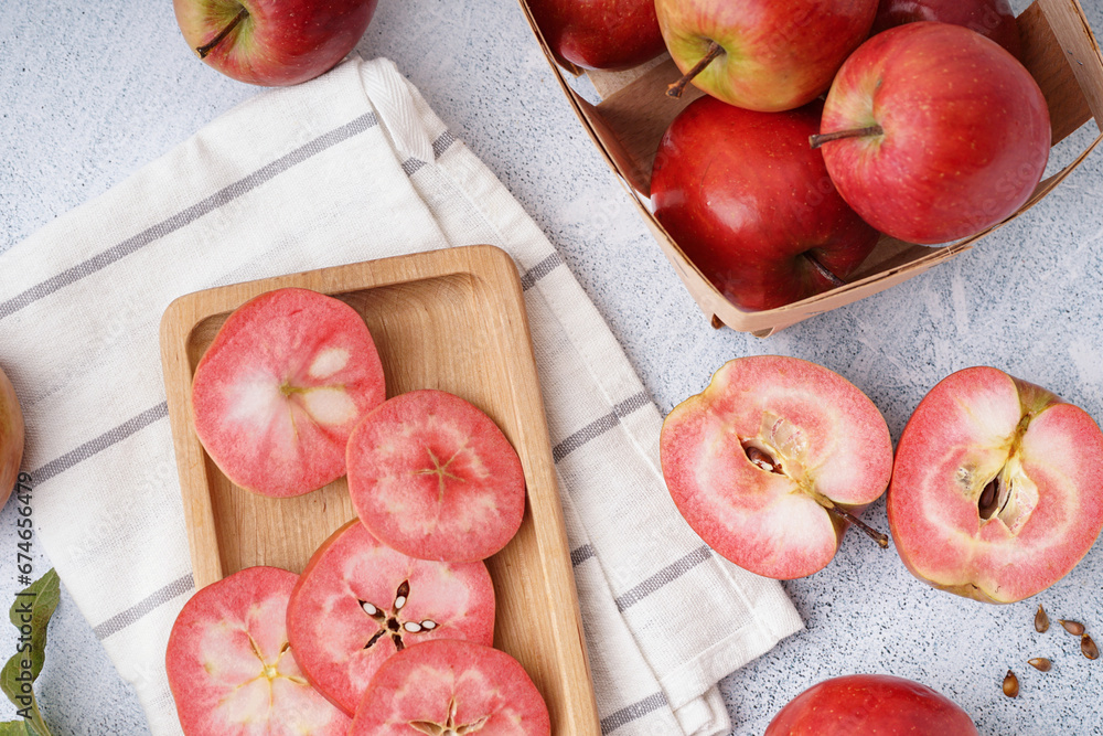 Wooden board and basket with sweet pink apples on white background