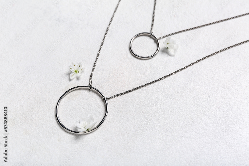 Silver necklaces with flowers on white background, closeup