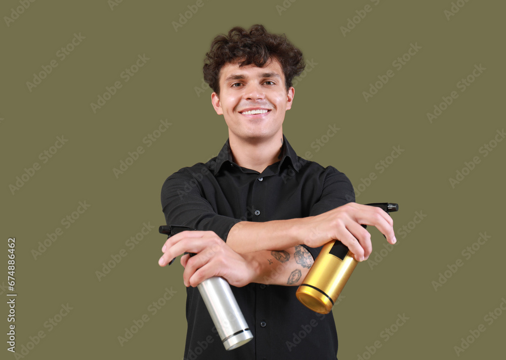 Handsome young man with bottles of hair spray on green background