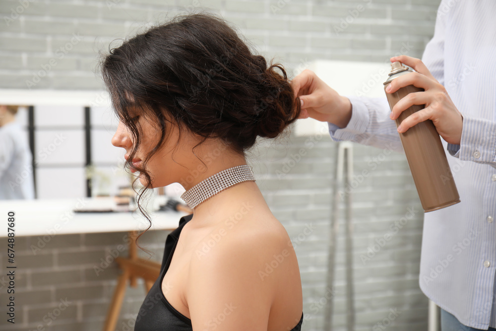 Professional hairdresser applying hair spray on young womans hair in beauty salon