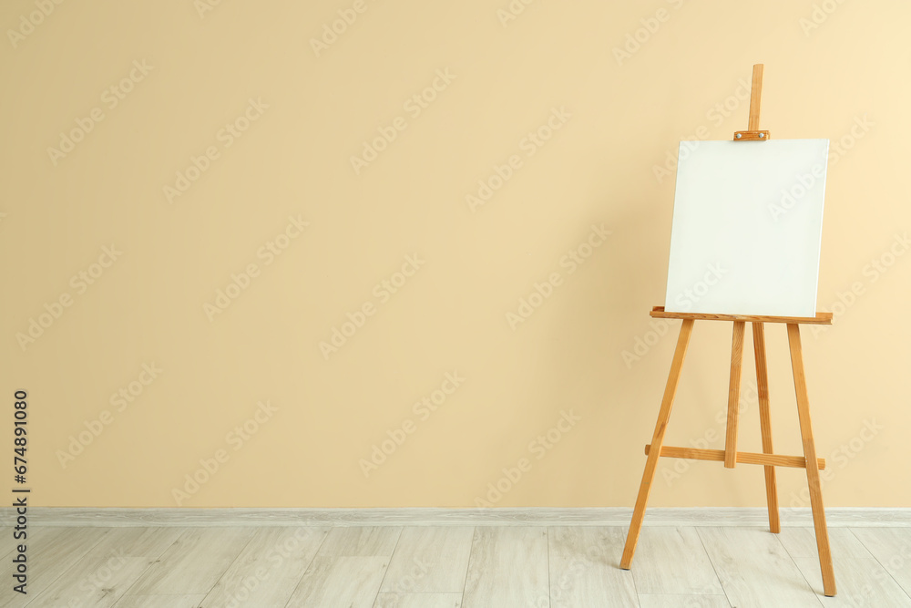 Wooden easel with blank canvas near beige wall