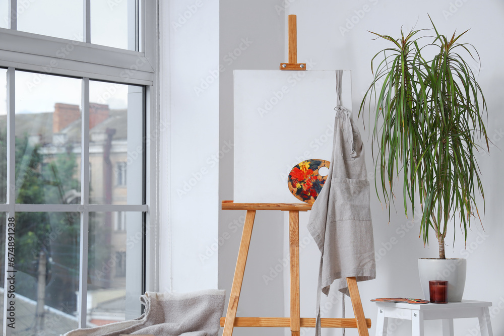 Wooden easel with blank canvas near white wall