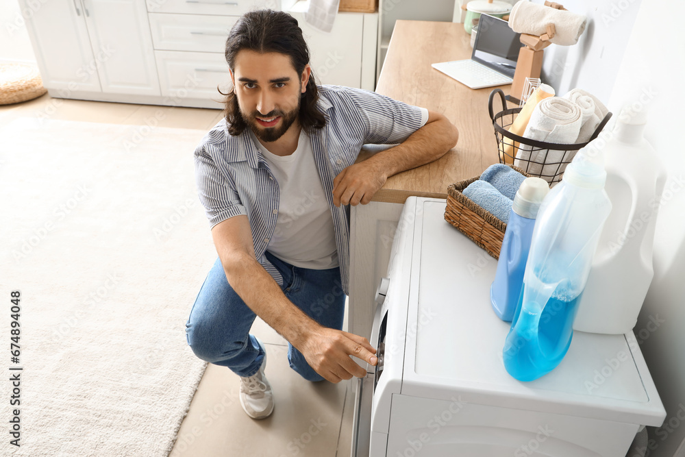 Young man switching on washing machine at home