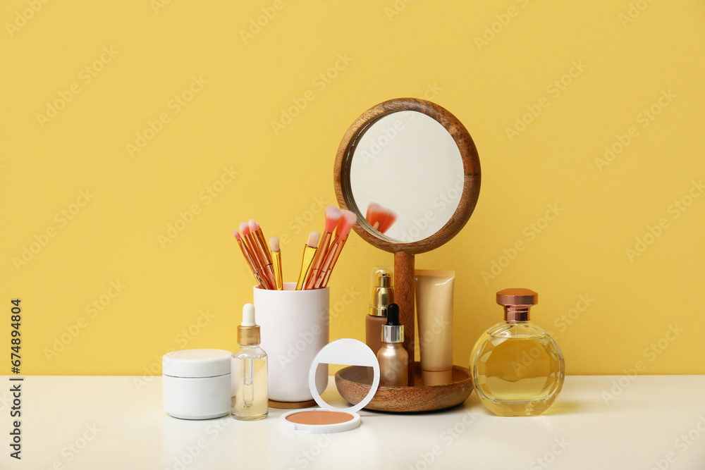 Different makeup products and mirror on dressing table near beige wall in room