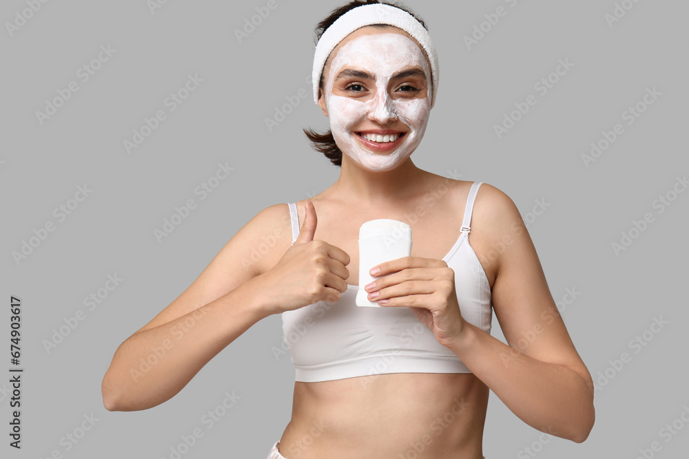 Young woman with deodorant showing thumb-up on light background