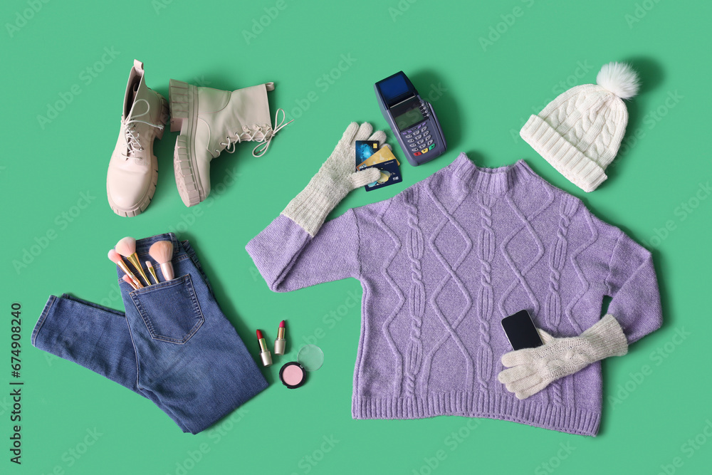 Winter clothes with accessories, payment terminal and credit cards on green background