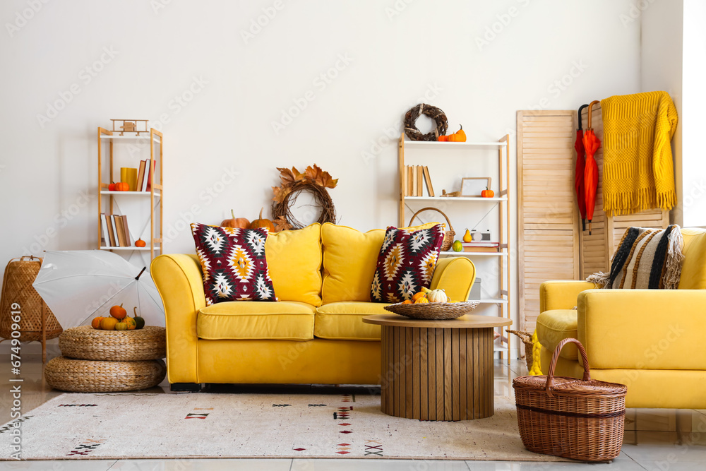 Interior of living room with yellow sofa, coffee table, autumn leaves and pumpkins