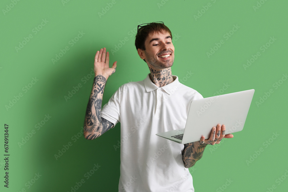 Happy young man with modern laptop on green background