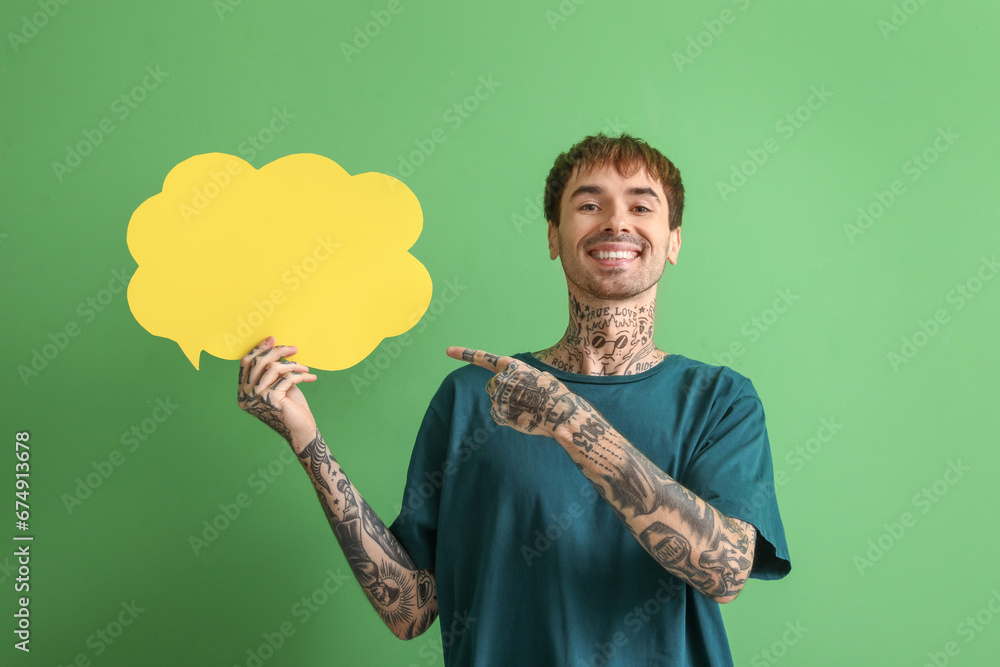 Happy young man pointing at blank speech bubble on green background