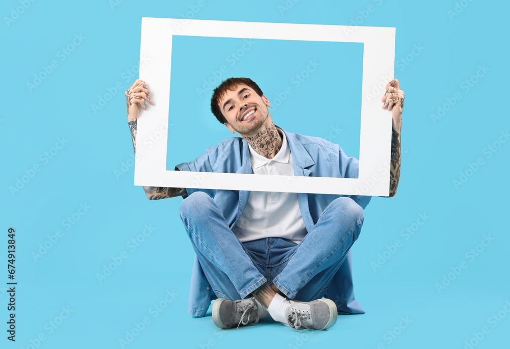 Happy young man holding white photo frame on blue background