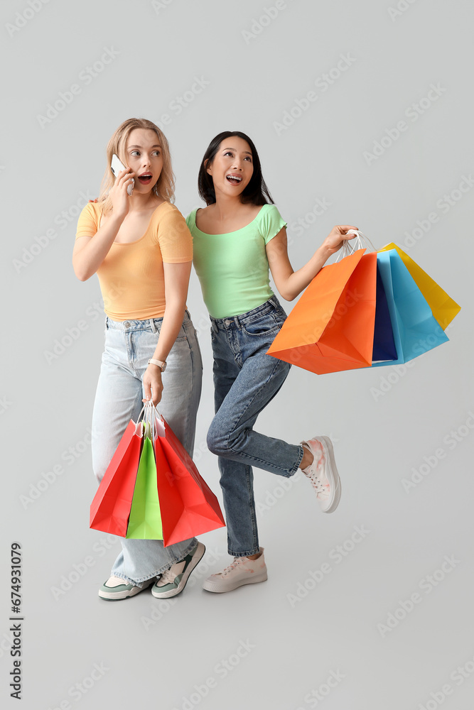 Beautiful young women holding shopping bags and talking by mobile phone on white background