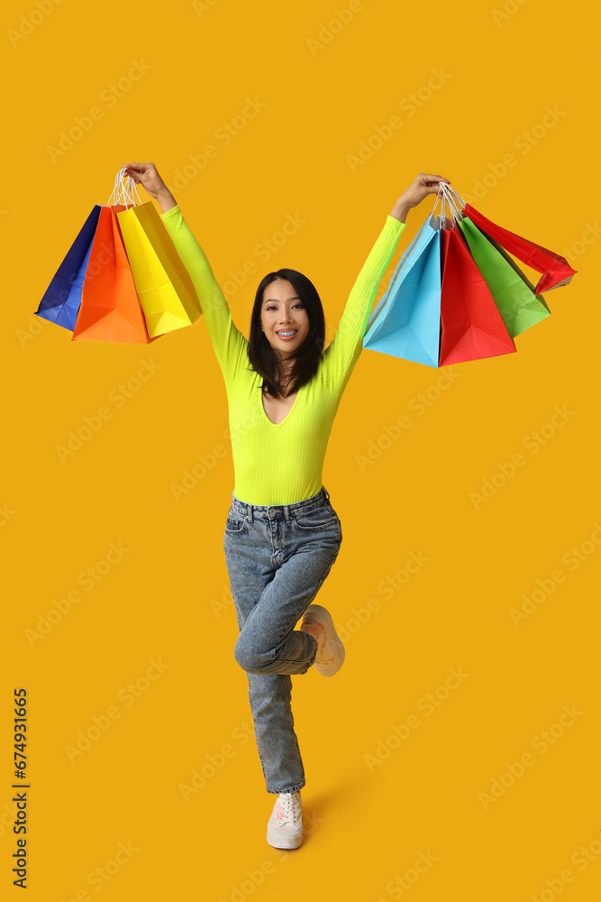 Young Asian woman with shopping bags on yellow background