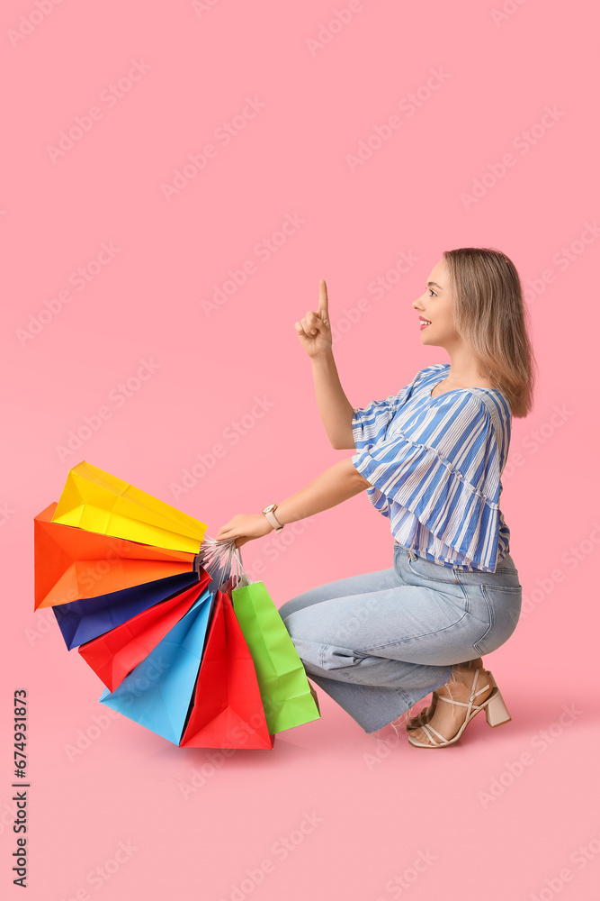 Young woman with shopping bags on pink background