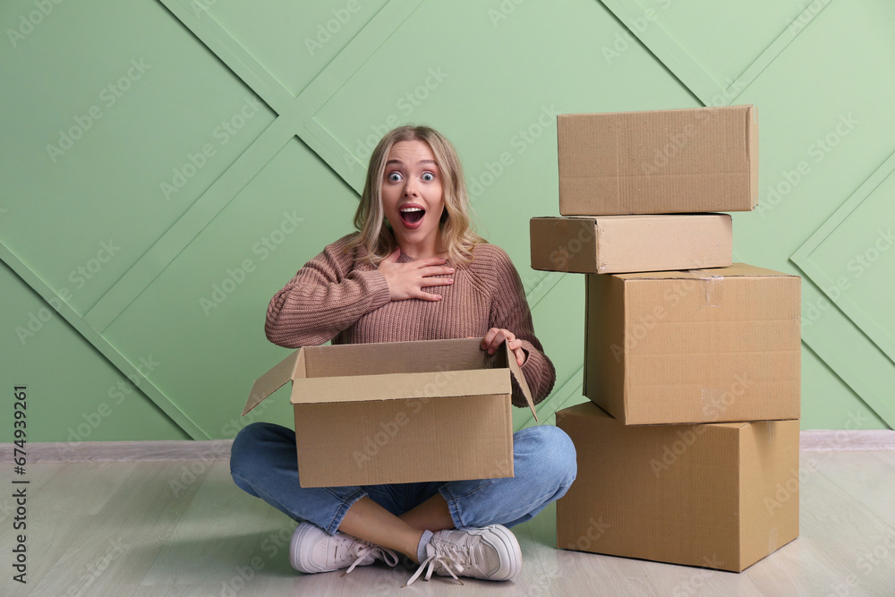 Emotional young woman with cardboard boxes on green background