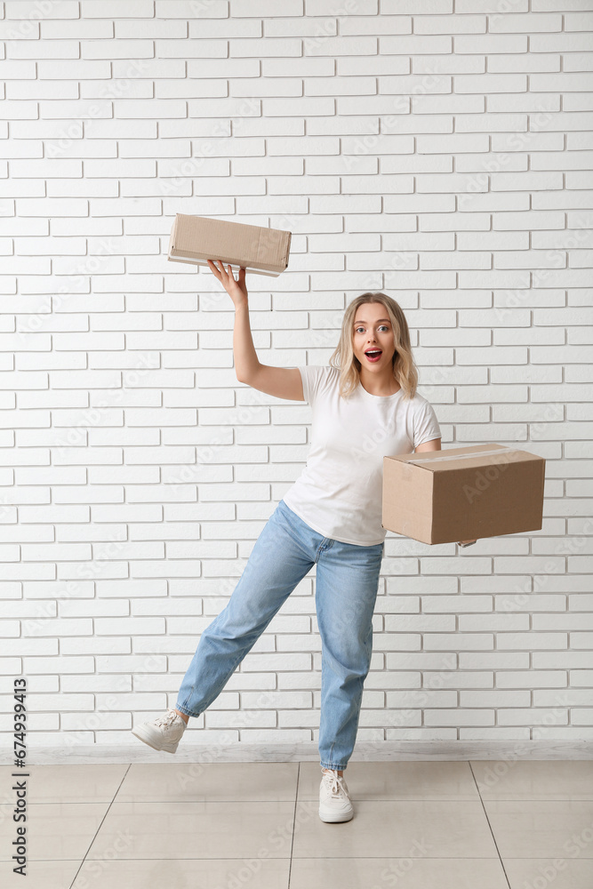 Young woman with cardboard boxes on white brick background