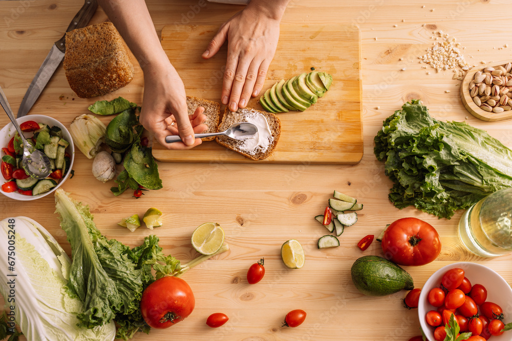 Lady spreading sauce on bread for vegetarian sandwich on wooden table.