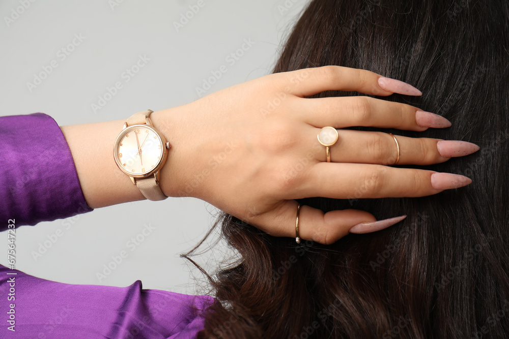 Elegant young woman with wristwatch on grey background, back view